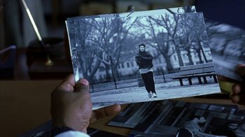 Movie still from “The Siege” (1998), directed by Edward Zwick – A person holding an old photo of a woman in a park; Medium shot, Over the shoulder angle
