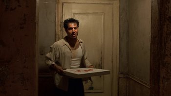 Movie still from “The Siege” (1998), directed by Edward Zwick – A man holding a box of pizza in a room; Medium shot, Low angle
