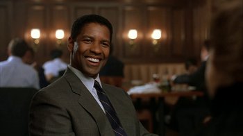 Movie still from “The Siege” (1998), directed by Edward Zwick – A man wearing a suit and tie smiling for the camera; Close Up shot, Low angle