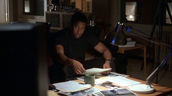 Movie still from “The Siege” (1998), directed by Edward Zwick – A man sitting at a table looking at a piece of paper; Medium shot, High angle