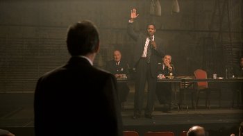 Movie still from “The Siege” (1998), directed by Edward Zwick – A man in a suit and tie standing in front of three other men; Medium shot, Over the shoulder angle