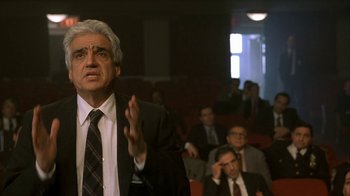 Movie still from “The Siege” (1998), directed by Edward Zwick – An older man in a suit and tie in front of a group of people; Close Up shot, Low angle