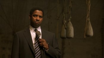 Movie still from “The Siege” (1998), directed by Edward Zwick – A man in a suit and tie holding a microphone; Close Up shot, Over the shoulder angle