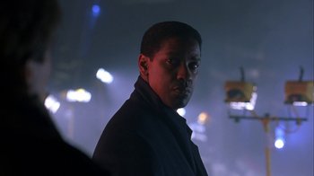 Movie still from “The Siege” (1998), directed by Edward Zwick – A man standing in the dark in front of a building; Close Up shot, Over the shoulder angle