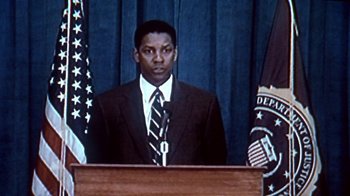Movie still from “The Siege” (1998), directed by Edward Zwick – A man standing at a podium in front of two flags; Close Up shot, Low angle