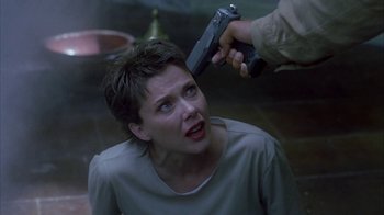 Movie still from “The Siege” (1998), directed by Edward Zwick – A woman getting her hair cut by a man with a gun in her hand; Close Up shot, Over the shoulder angle