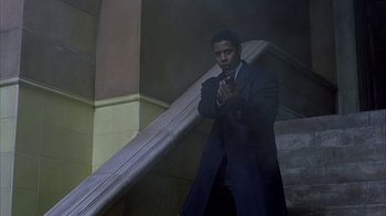 Movie still from “The Siege” (1998), directed by Edward Zwick – A man standing on a stair case in a suit; Wide shot, Low angle