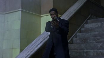 Movie still from “The Siege” (1998), directed by Edward Zwick – A man in a black coat standing in front of a staircase; Medium shot, Low angle