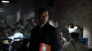Movie still from “The Siege” (1998), directed by Edward Zwick – A man in a suit and tie holding a book in his hands; Medium shot, Low angle