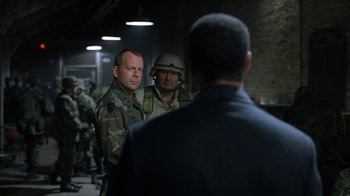 Movie still from “The Siege” (1998), directed by Edward Zwick – Two men in military fatigues are standing next to each other in front of a wall; Medium shot, Over the shoulder angle