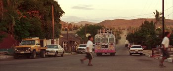 Movie still from “The Sisterhood of the Traveling Pants” (2005), directed by Ken Kwapis – A skateboarder crosses the street in front of a colorful bus; Extreme Wide shot, Low angle