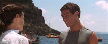 Movie still from “The Sisterhood of the Traveling Pants” (2005), directed by Ken Kwapis – A young man smiles while standing in front of a body of water; Close Up shot, Over the shoulder angle