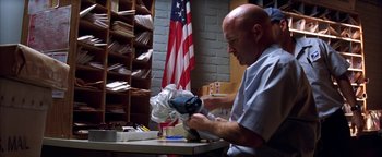 Movie still from “The Sisterhood of the Traveling Pants” (2005), directed by Ken Kwapis – A man working in a room in front of an american flag; Medium shot, Low angle