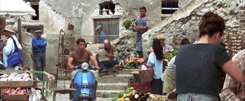 Movie still from “The Sisterhood of the Traveling Pants” (2005), directed by Ken Kwapis – A group of people sitting on steps near a pile of food; Wide shot, High angle