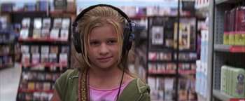 Movie still from “The Sisterhood of the Traveling Pants” (2005), directed by Ken Kwapis – A young girl wearing headphones in front of a store; Close Up shot, Over the shoulder angle