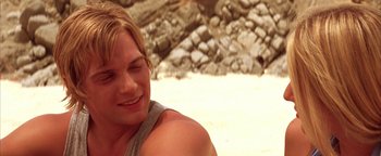 Movie still from “The Sisterhood of the Traveling Pants” (2005), directed by Ken Kwapis – A man sitting on top of a beach next to a pile of rocks; Close Up shot, Over the shoulder angle