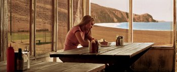 Movie still from “The Sisterhood of the Traveling Pants” (2005), directed by Ken Kwapis – A woman sitting at a wooden table with a drink in front of a window; Wide shot, Over the shoulder angle