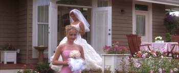 Movie still from “The Sisterhood of the Traveling Pants” (2005), directed by Ken Kwapis – Two young women in wedding dresses standing in front of a house; Medium shot, Over the shoulder angle