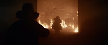 Movie still from “The Sisters Brothers” (2018), directed by Jacques Audiard – A person is standing in front of a fire; Wide shot, Over the shoulder angle