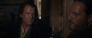 Movie still from “The Sisters Brothers” (2018), directed by Jacques Audiard – A man sitting in front of a bottle of wine; Close Up shot, Low angle