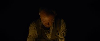 Movie still from “The Sisters Brothers” (2018), directed by Jacques Audiard – An old man sitting in the dark looking down; Close Up shot, Overhead angle
