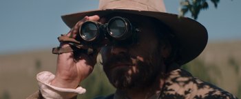 Movie still from “The Sisters Brothers” (2018), directed by Jacques Audiard – A man looking through a pair of binoculars; Close Up shot, Over the shoulder angle