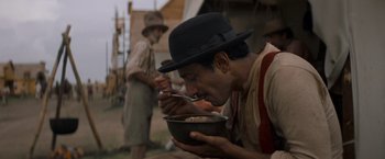 Movie still from “The Sisters Brothers” (2018), directed by Jacques Audiard – A man wearing a black hat eating something from a bowl; Medium shot, High angle