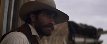 Movie still from “The Sisters Brothers” (2018), directed by Jacques Audiard – A person wearing a hat with a horse in the background; Close Up shot, Over the shoulder angle