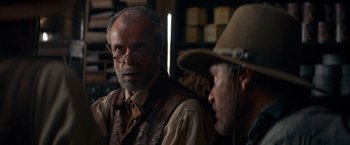 Movie still from “The Sisters Brothers” (2018), directed by Jacques Audiard – A man with a beard wearing a hat and glasses; Close Up shot, Over the shoulder angle
