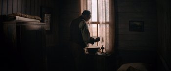 Movie still from “The Sisters Brothers” (2018), directed by Jacques Audiard – A man standing in front of a window with a bowl of food; Medium shot, Over the shoulder angle