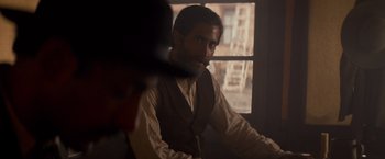 Movie still from “The Sisters Brothers” (2018), directed by Jacques Audiard – A man sitting in front of a window in a room; Medium shot, Over the shoulder angle