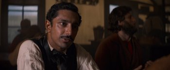 Movie still from “The Sisters Brothers” (2018), directed by Jacques Audiard – A person wearing a suit and a tie; Close Up shot, Over the shoulder angle