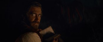 Movie still from “The Sisters Brothers” (2018), directed by Jacques Audiard – A person holding a book in a dark room; Close Up shot, Over the shoulder angle