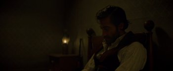 Movie still from “The Sisters Brothers” (2018), directed by Jacques Audiard – A man sitting in a chair in a dark room; Close Up shot, Over the shoulder angle