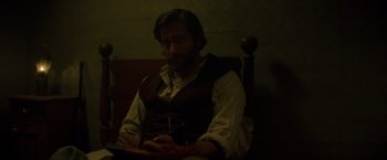 Movie still from “The Sisters Brothers” (2018), directed by Jacques Audiard – A man sitting in a chair looking at his cell phone; Medium shot, High angle