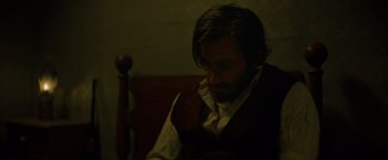 Movie still from “The Sisters Brothers” (2018), directed by Jacques Audiard – A man sitting in front of a wooden table; Close Up shot, Low angle