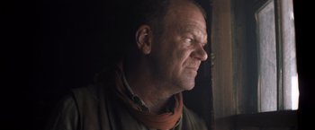 Movie still from “The Sisters Brothers” (2018), directed by Jacques Audiard – An older man wearing a neck scarf looking out of a window; Close Up shot, Low angle
