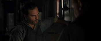 Movie still from “The Sisters Brothers” (2018), directed by Jacques Audiard – A bearded man leaning up against a wall; Close Up shot, Over the shoulder angle