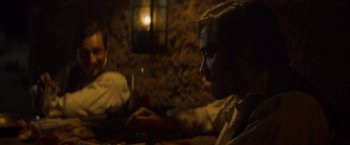 Movie still from “The Sisters Brothers” (2018), directed by Jacques Audiard – A man sitting at a table with a glass of red wine; Medium shot, Over the shoulder angle