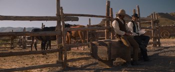 Movie still from “The Sisters Brothers” (2018), directed by Jacques Audiard – A man sitting on top of a wooden fence next to cows; Wide shot, Low angle