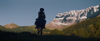 Movie still from “The Sisters Brothers” (2018), directed by Jacques Audiard – A man riding a horse in a field with mountains in the background; Wide shot, Low angle