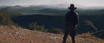 Movie still from “The Sisters Brothers” (2018), directed by Jacques Audiard – A man standing on top of a hill looking at the mountains; Wide shot, Low angle