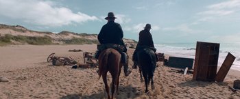 Movie still from “The Sisters Brothers” (2018), directed by Jacques Audiard – Two people riding horses on a beach near the ocean; Wide shot, Low angle