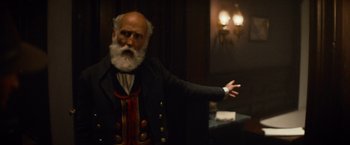 Movie still from “The Sisters Brothers” (2018), directed by Jacques Audiard – An old man with a long beard is standing in front of a wall; Medium shot, Over the shoulder angle