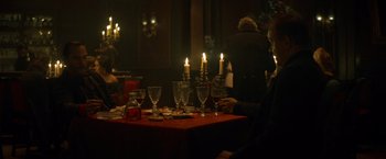 Movie still from “The Sisters Brothers” (2018), directed by Jacques Audiard – A group of people sitting around a table with candles; Medium shot, Over the shoulder angle