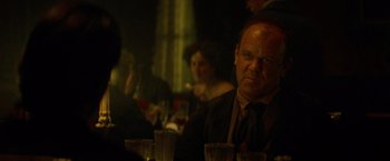 Movie still from “The Sisters Brothers” (2018), directed by Jacques Audiard – A man sitting at a table with a glass in front of him; Close Up shot, Over the shoulder angle