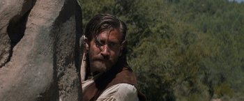 Movie still from “The Sisters Brothers” (2018), directed by Jacques Audiard – A person wearing a vest near a tree; Close Up shot, Over the shoulder angle