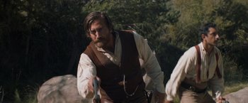 Movie still from “The Sisters Brothers” (2018), directed by Jacques Audiard – A man in a brown vest holding a gun in his hand; Medium shot, Over the shoulder angle
