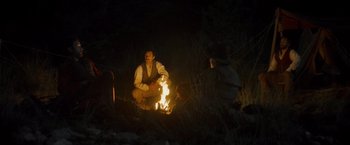 Movie still from “The Sisters Brothers” (2018), directed by Jacques Audiard – A man sitting in front of a fire at night; Wide shot, High angle