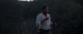 Movie still from “The Sisters Brothers” (2018), directed by Jacques Audiard – A man in a white shirt holding a knife and a fork; Medium shot, Over the shoulder angle